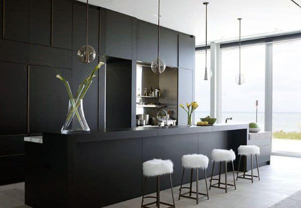 Modern black kitchen with sleek cabinets, pendant lights, and white fur bar stools.