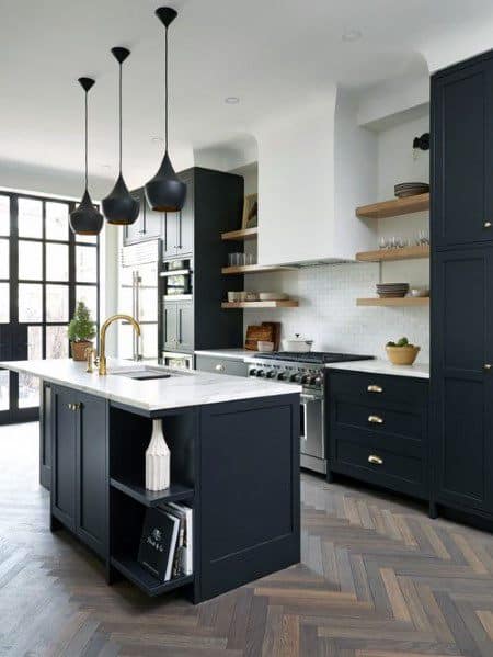 Black kitchen cabinets with gold hardware, open shelves, and chevron-pattern hardwood flooring.