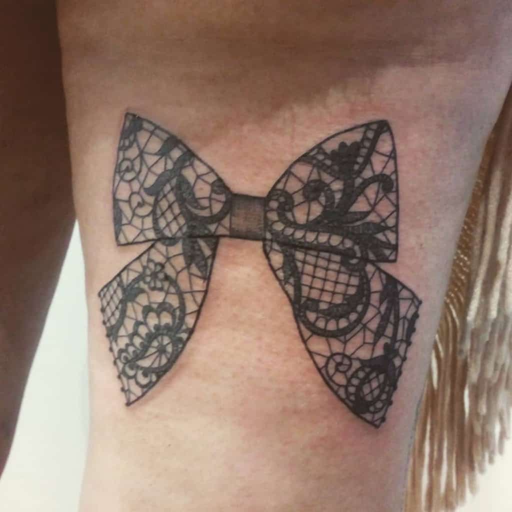 Black lace bow tattoo with intricate floral and filigree patterns, creating a delicate and elegant design on the thigh.
