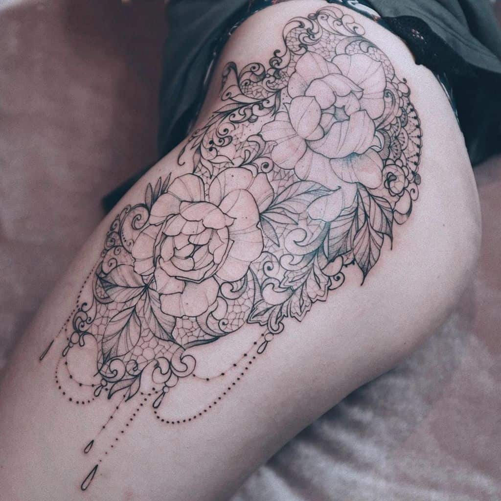 Thigh tattoo featuring intricate floral designs with lace patterns, delicate beaded chains, and ornamental filigree details.