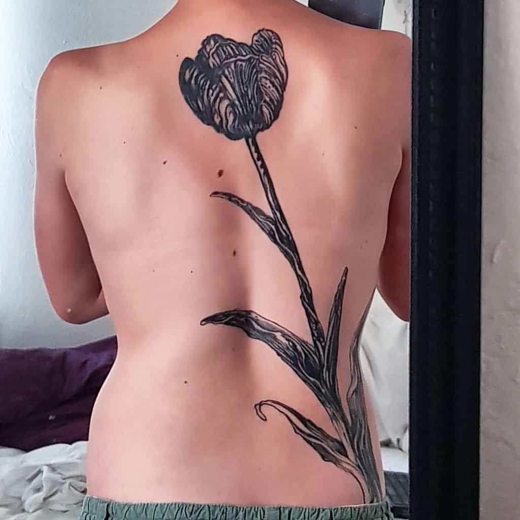 A large, detailed black tulip tattoo covering the back, with intricate shading on the flower and long, elegant leaves extending down the spine.