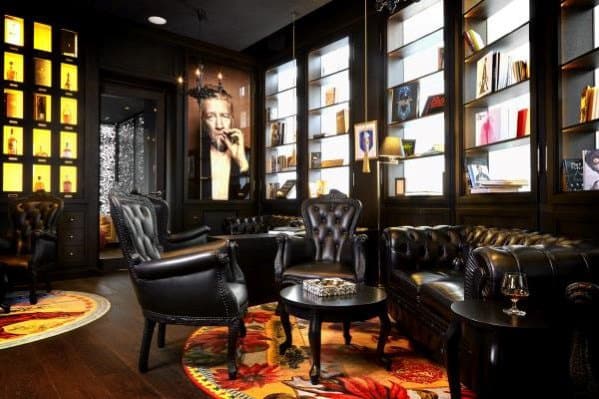 Elegant man cave with black leather chairs, dark bookshelves, and lit displays; a portrait hangs on the wall