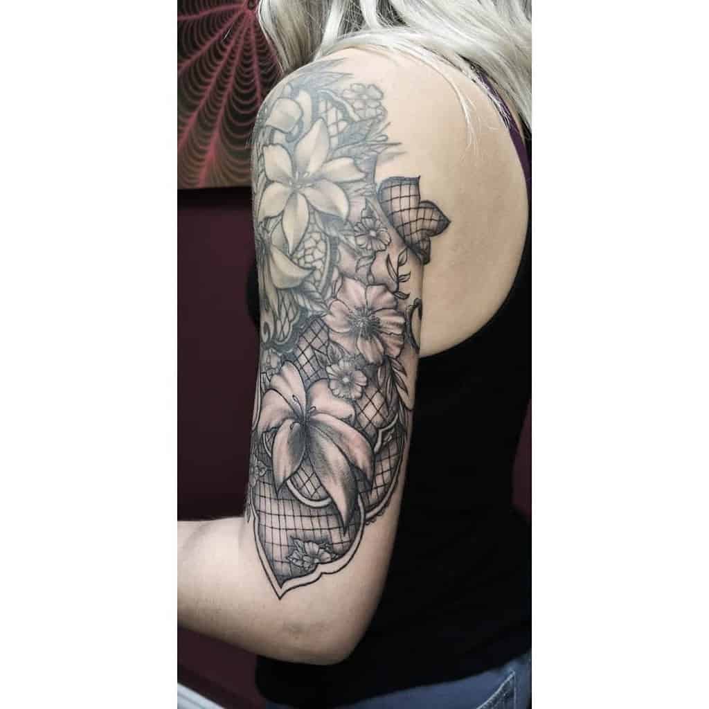 Elegant black and grey lace tattoo sleeve with detailed floral patterns, netting, and ornamental elements for a soft yet bold look.