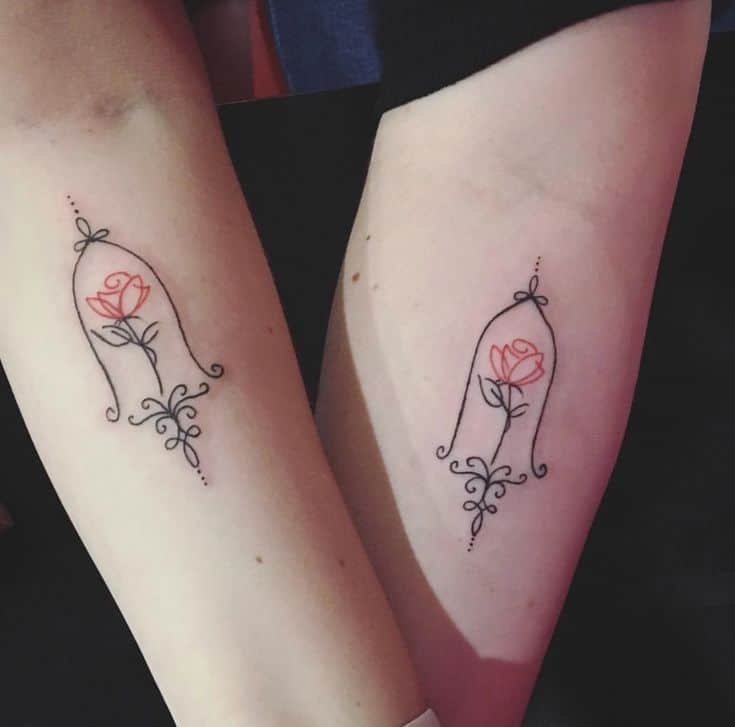 Matching minimalist tattoos of the enchanted rose inside an ornate glass dome, featuring fine-line details and delicate red ink accents.