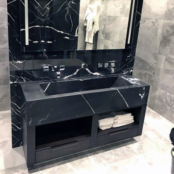 Black marble vanity with sleek modern design, large mirror, and open shelving for towels.