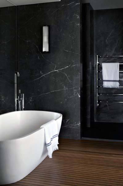 Elegant bathroom with black marble walls, freestanding white tub, and wooden flooring.