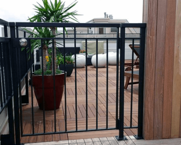 Rooftop deck with plants, chairs, and bean bags beyond a black metal gate