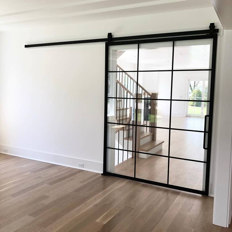 Black metal French-style sliding barn door with glass panes dividing a modern living space from a staircase area.