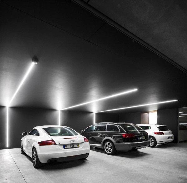Modern garage with black ceiling, LED strip lighting, and sleek luxury cars parked inside.