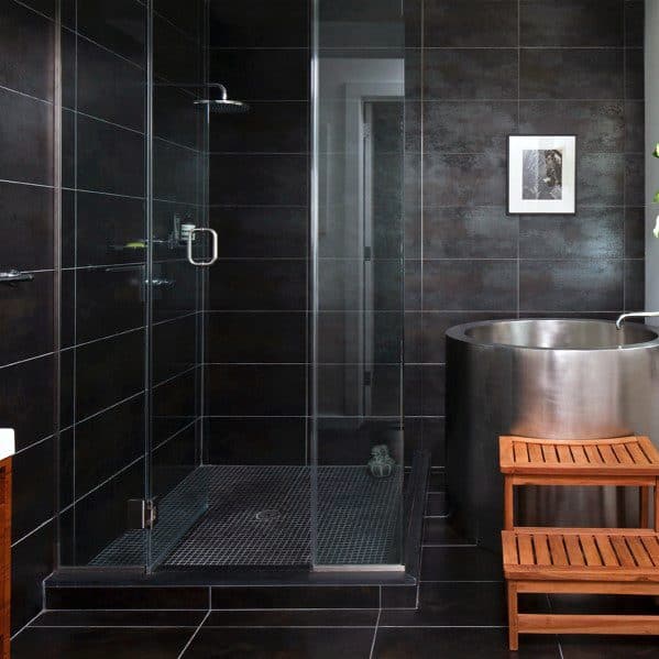 Modern bathroom with dark tiles, a glass shower, wooden bench, and metal floor