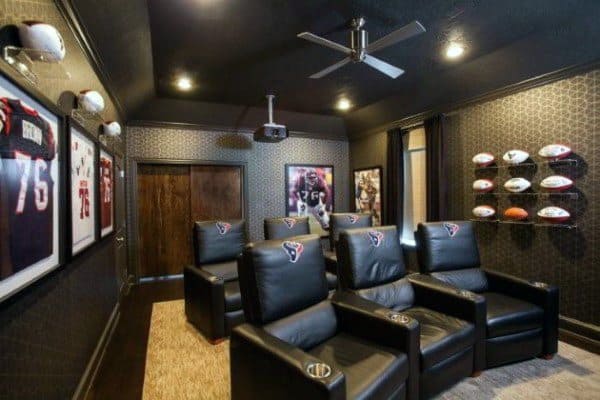 Sports-themed home theater with black walls, leather recliners, and mounted memorabilia displays.