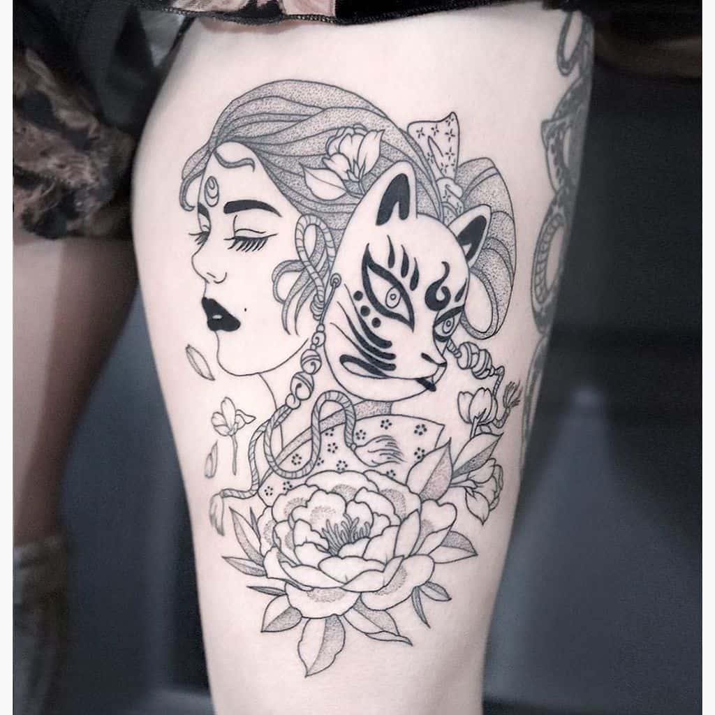 Black and gray tattoo of a woman with flowing hair, a kitsune mask, floral elements, and intricate ribbon details for a mystical look.