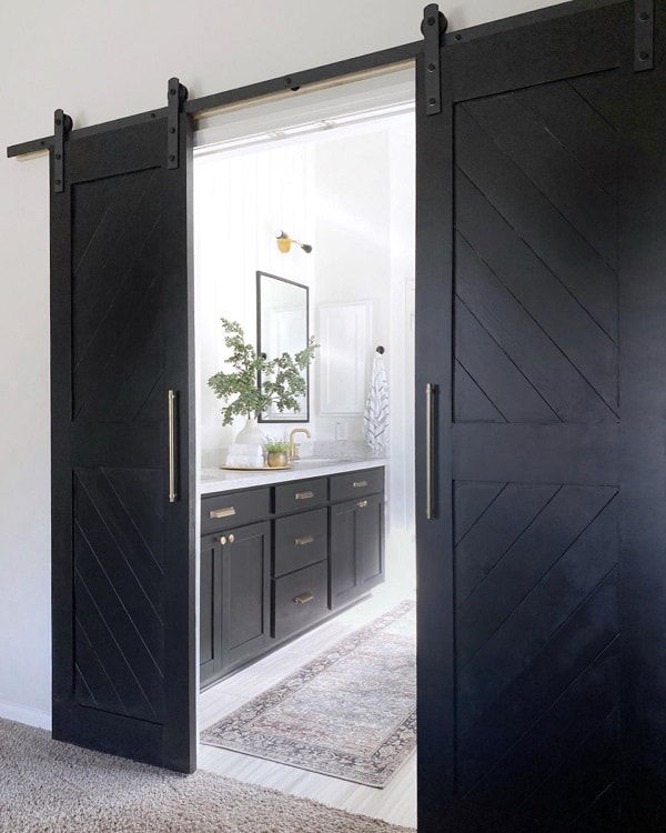 Large black sliding barn doors leading to a modern bathroom with black cabinetry and gold accents.