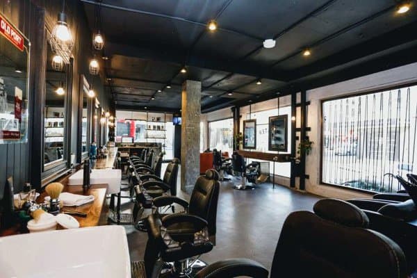 Barbershop with black ceiling, industrial decor, and spacious layout with large windows.