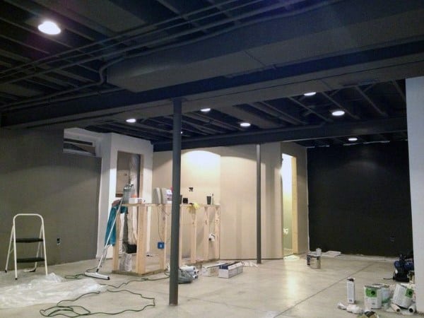 Basement under renovation with black exposed ceiling, recessed lighting, and unfinished walls.
