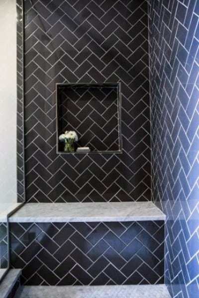 Black herringbone patterned tile shower with built-in niche and marble bench.