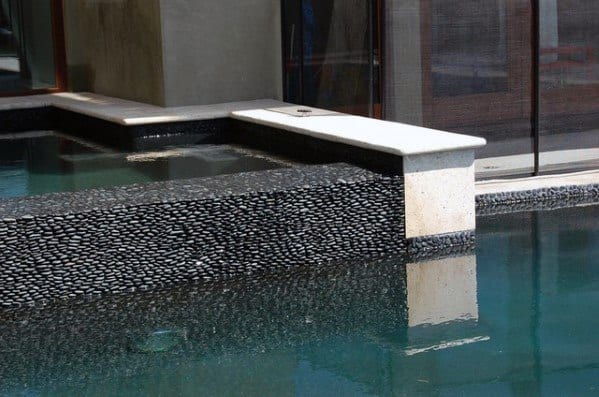 Black pebble stone pool tiles with a sleek waterline design and modern stone accents.
