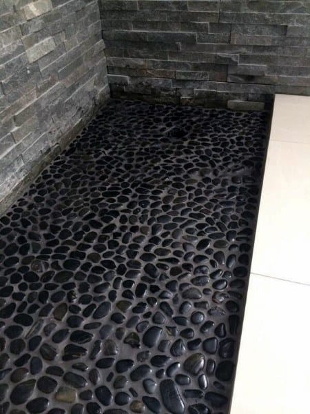 Shower floor with black pebble stones and dark textured stone walls.