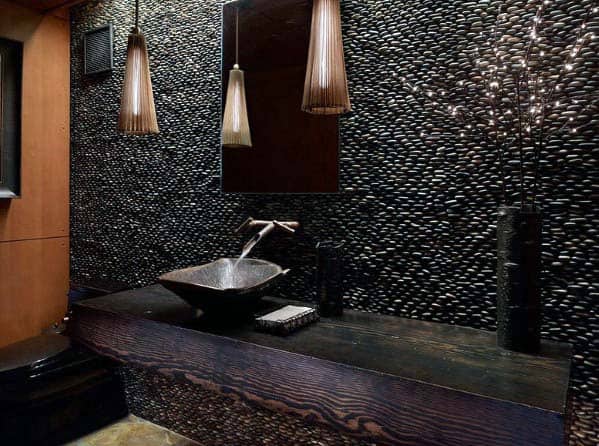 Black pebble tile wall bathroom with wood vanity and stylish pendant lighting.