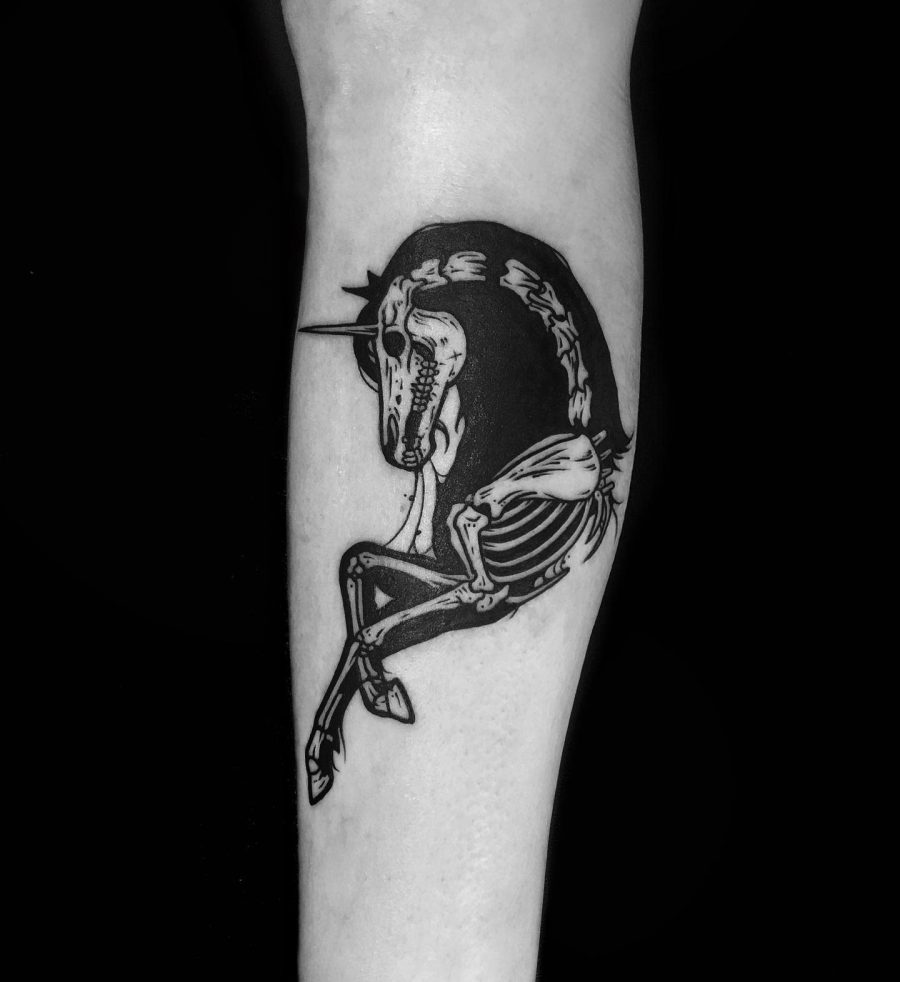 Bold black ink tattoo of a skeletal unicorn curled in a circular shape, blending gothic and surreal elements for a dark, mystical design.