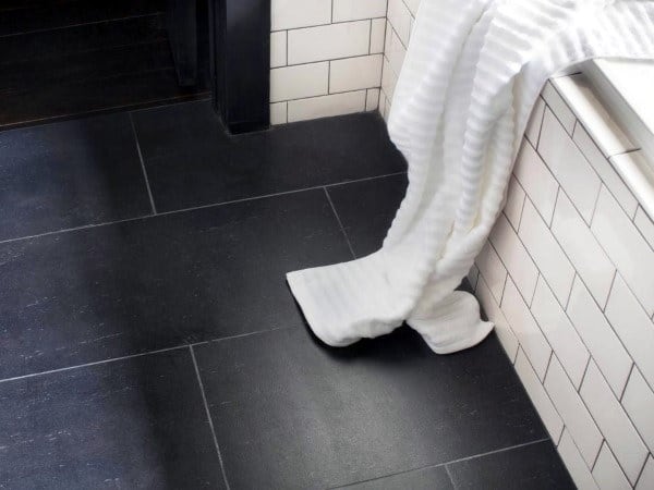 Black slate bathroom floor tiles with white subway wall tiles and a draped white towel.