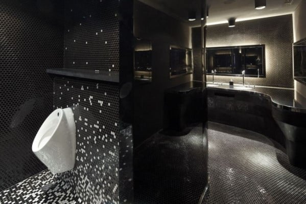 Black tiled bathroom with white urinal and sleek modern lighting.