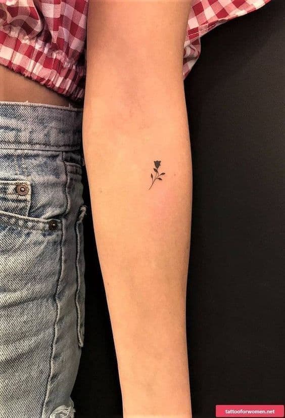 A tiny black tulip tattoo on the inner forearm, featuring a delicate stem with small leaves in a minimalist fine-line design.