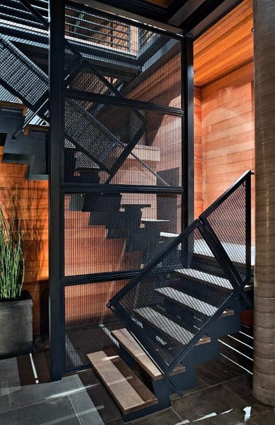 Modern staircase with black metal mesh railings, wooden steps, and a potted plant enhancing the industrial vibe