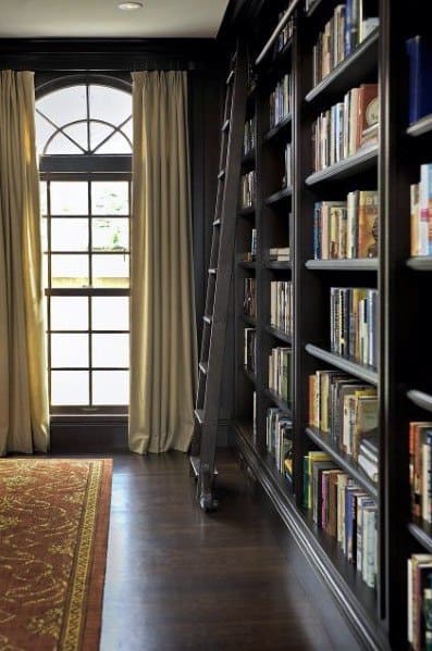 A cozy library with tall bookshelves, ladder, window, and flowing curtains