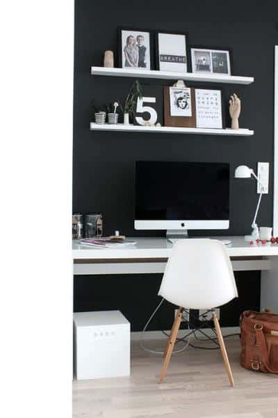 Minimalist workspace with a white chair, computer, and decorative shelves on a black wall