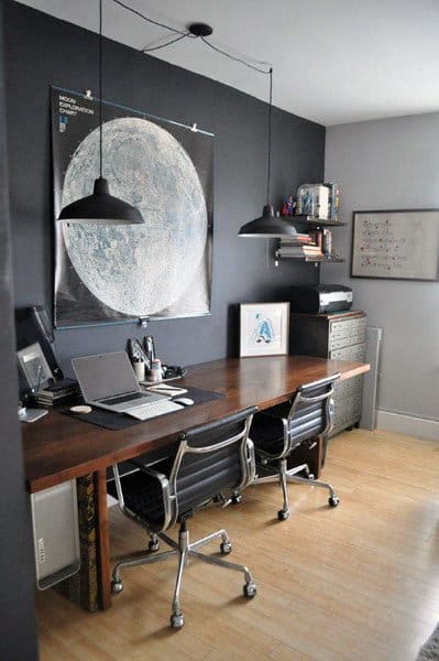 Modern office with a wooden desk, two chairs, computers, and a large moon poster on the wall