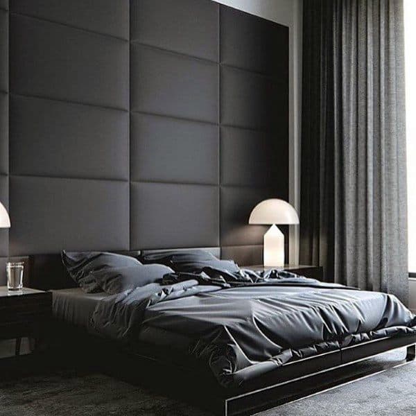 Modern black bedroom with tufted wall paneling, dark bedding, and sleek bedside lamps.