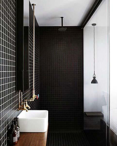 Modern bathroom with black tiled walls, brass fixtures, and a glass shower enclosure.