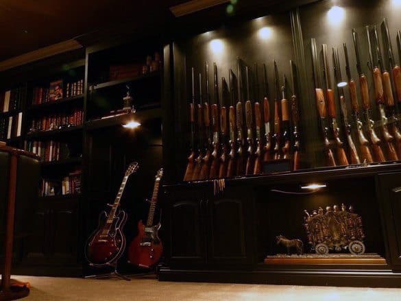 Moody gun room with black cabinetry, spotlighted rifles, and guitars for a stylish touch.
