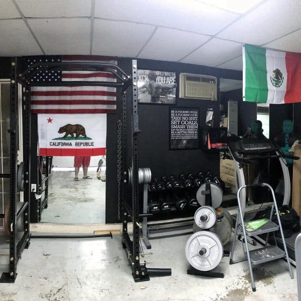 Garage gym with black walls, squat rack, dumbbells, weight plates, and cardio equipment.