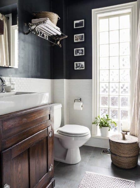 Charming half-bath with black walls, white subway tiles, wooden vanity, and a bright window.