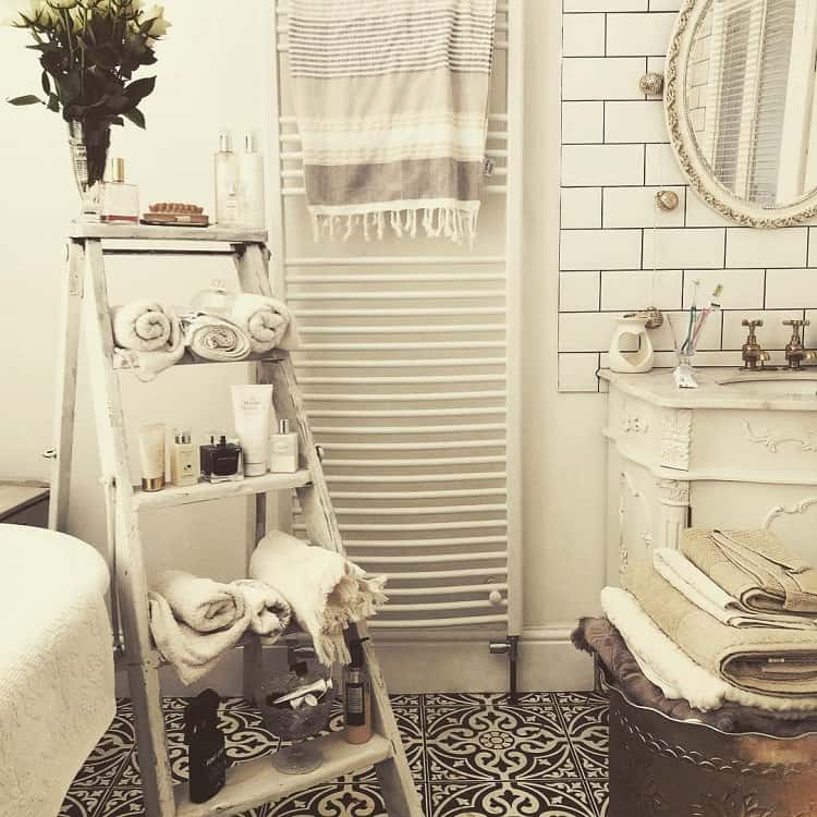 Farmhouse-style bathroom with floral tiles, a wooden ladder for towels, and a vintage vanity mirror