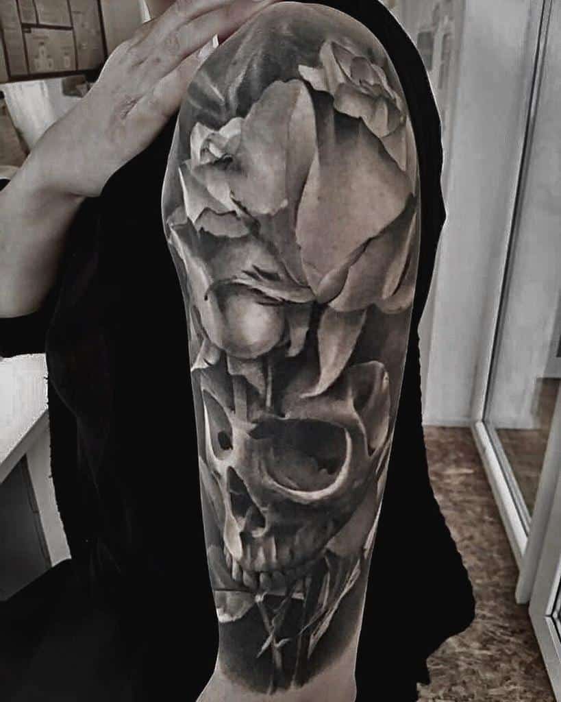 Black and grey realistic full-sleeve tattoo featuring a detailed skull and blooming roses, creating a striking contrast on the arm.