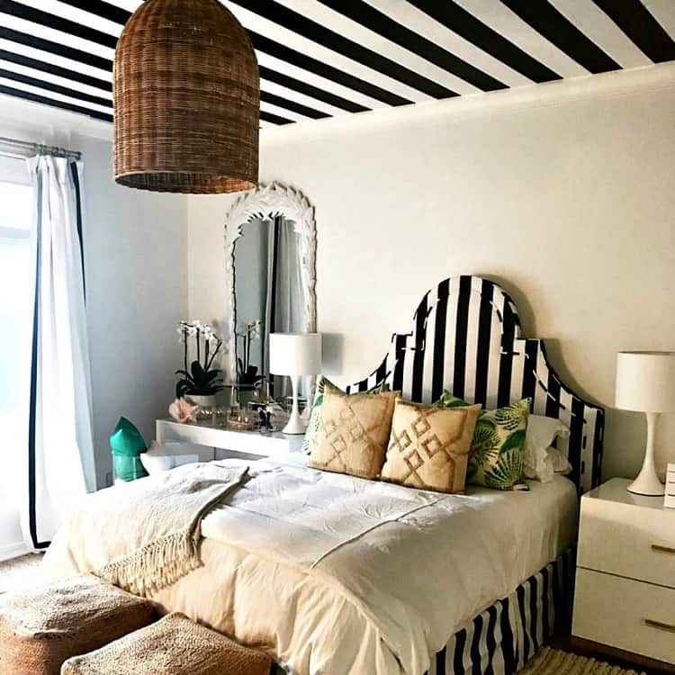 A stylish bedroom featuring a bold black-and-white striped ceiling, a wicker pendant light, and a mix of modern and natural textures, creating a unique and inviting atmosphere