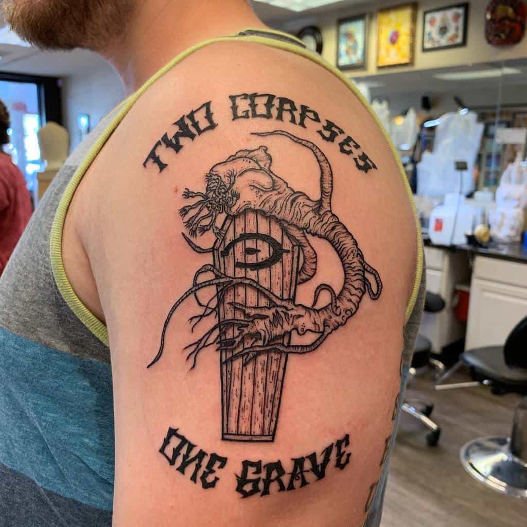 Black ink Halo-inspired tattoo featuring the Gravemind wrapped around a coffin with the phrase 'Two Corpses, One Grave,' inked on the upper arm.