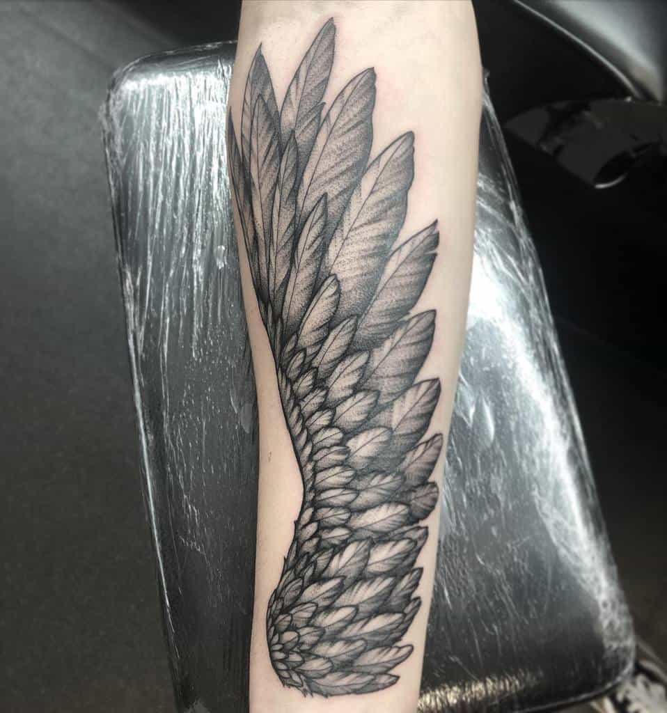 Tattoo of a detailed, monochrome angel wing with layered feathers