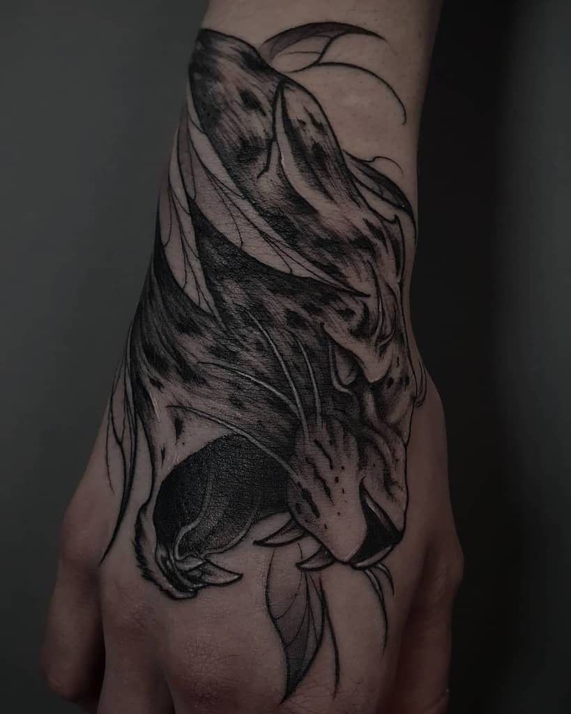 A dramatic black and grey tattoo of a jaguar's fierce expression, wrapping across the hand and wrist with dynamic flowing lines.