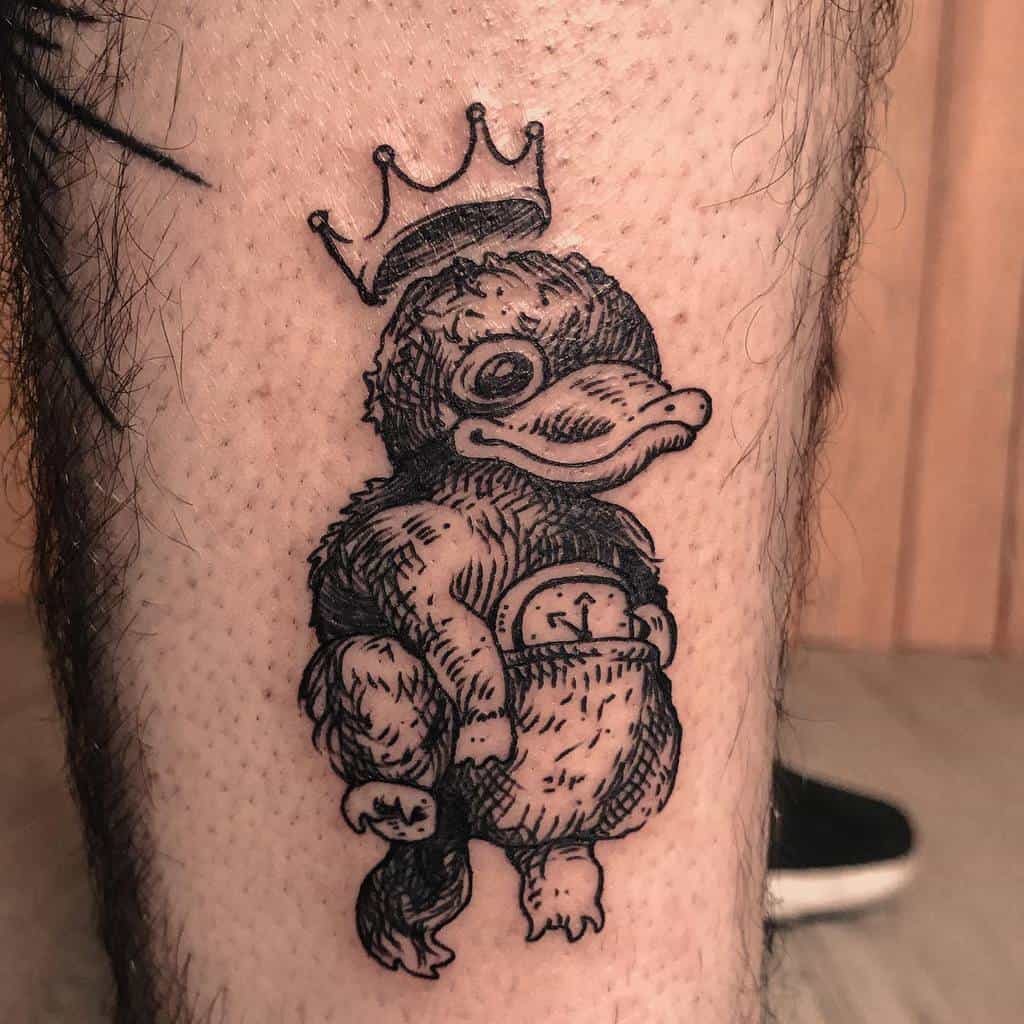 Detailed black ink tattoo of a Niffler from Fantastic Beasts, wearing a crown and holding treasures.