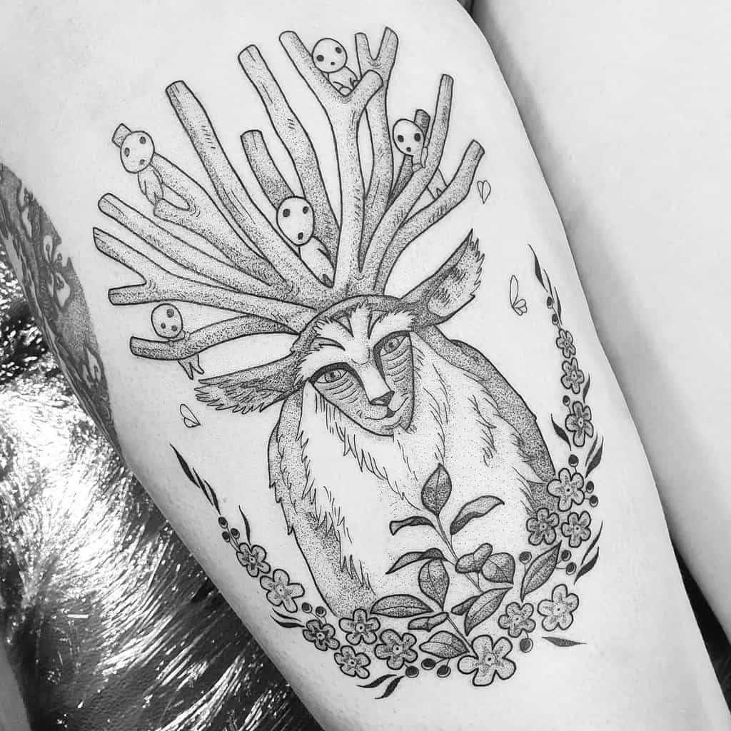 A detailed black and white tattoo of a deer with tree-like antlers. The antlers have small ghost-like figures scattered throughout, and the deer is surrounded by a floral design, creating a harmonious blend of nature and whimsical elements.