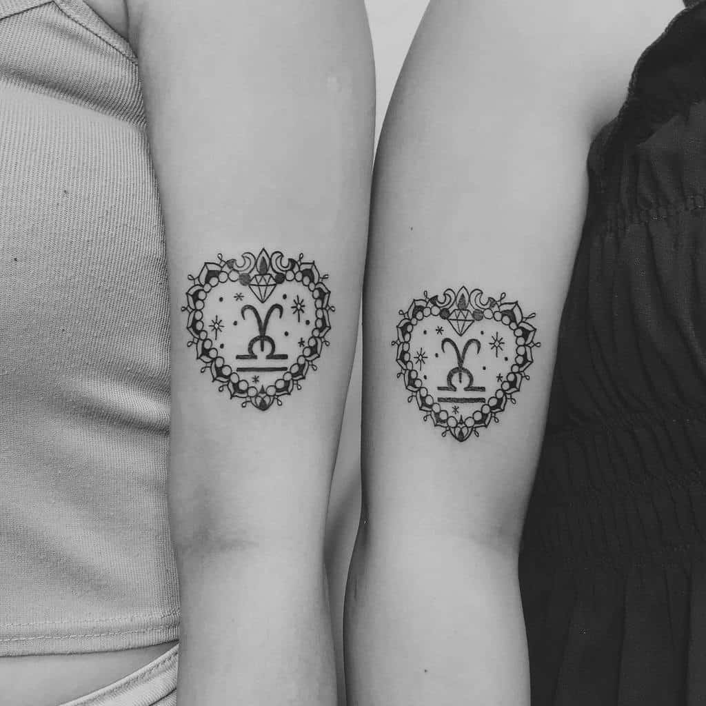 Matching sibling tattoos featuring intricate heart-shaped designs with Libra symbol, diamond, stars, and decorative lace-like borders