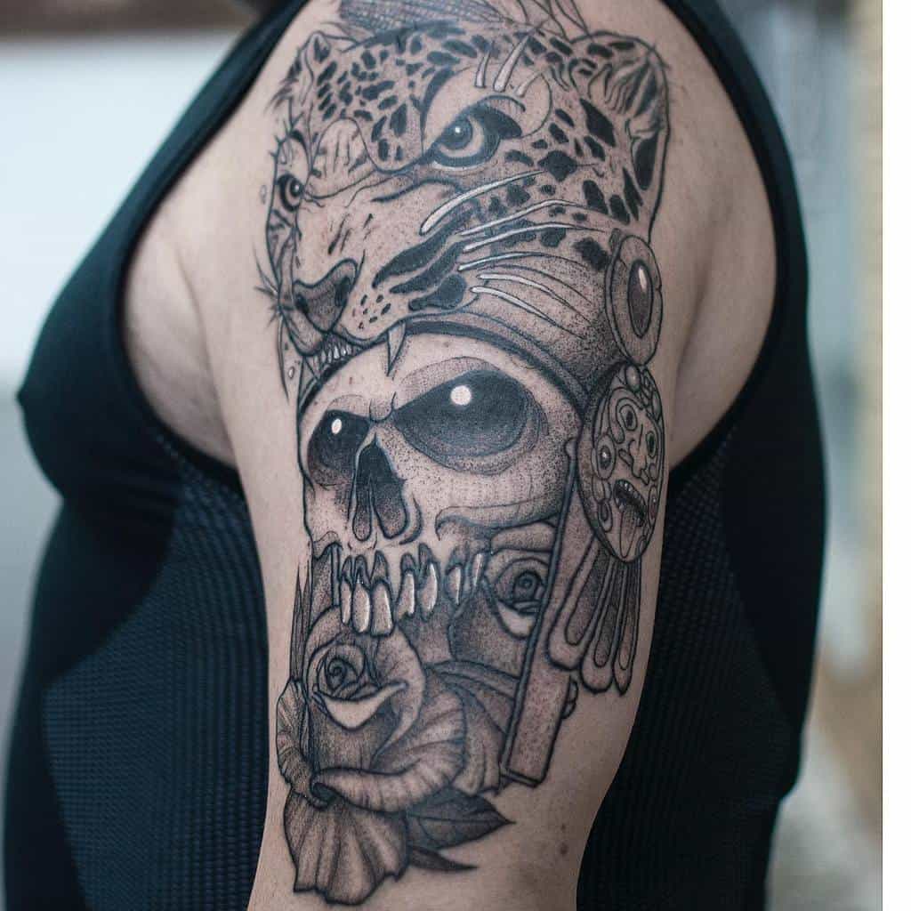 A detailed black and grey tattoo featuring a jaguar's face above a skull, with roses and intricate designs, covering the upper arm.