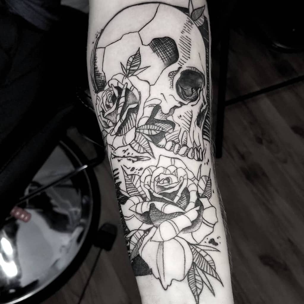 Black ink forearm tattoo of a skull with roses and intricate linework, featuring bold contrast and geometric shading.