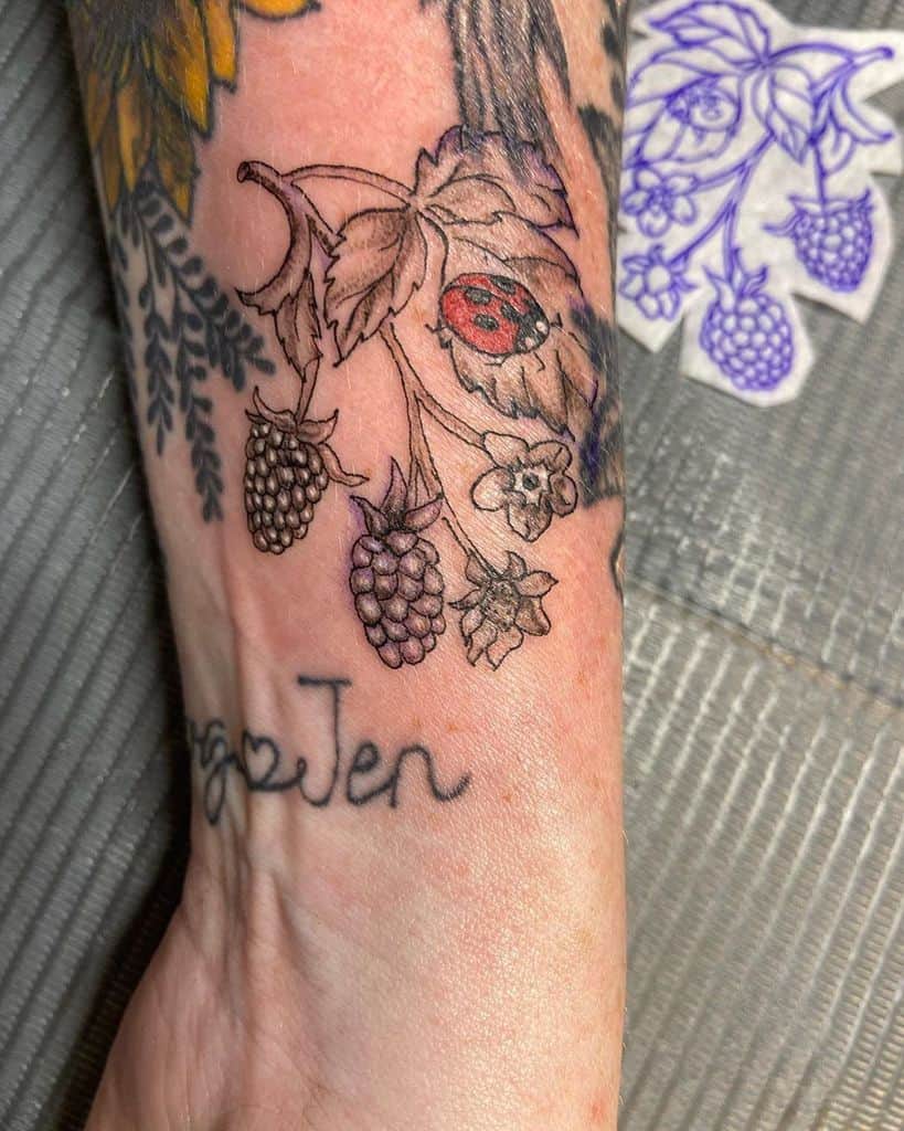Tattoo of a ladybug resting on a raspberry vine with detailed leaves and berries, blending fine linework and soft colors on the wrist.