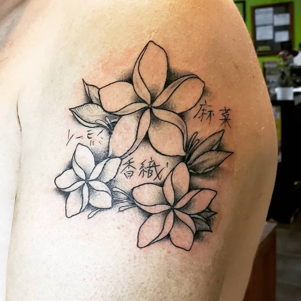 Tattoo of three plumeria flowers with Japanese kanji on the upper arm