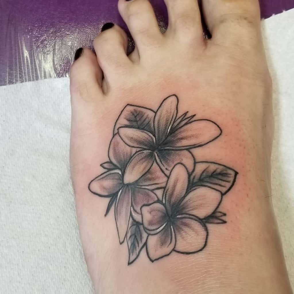 Black and gray Plumeria flower tattoo on the foot, featuring detailed shading and soft gradients to create a natural, elegant design